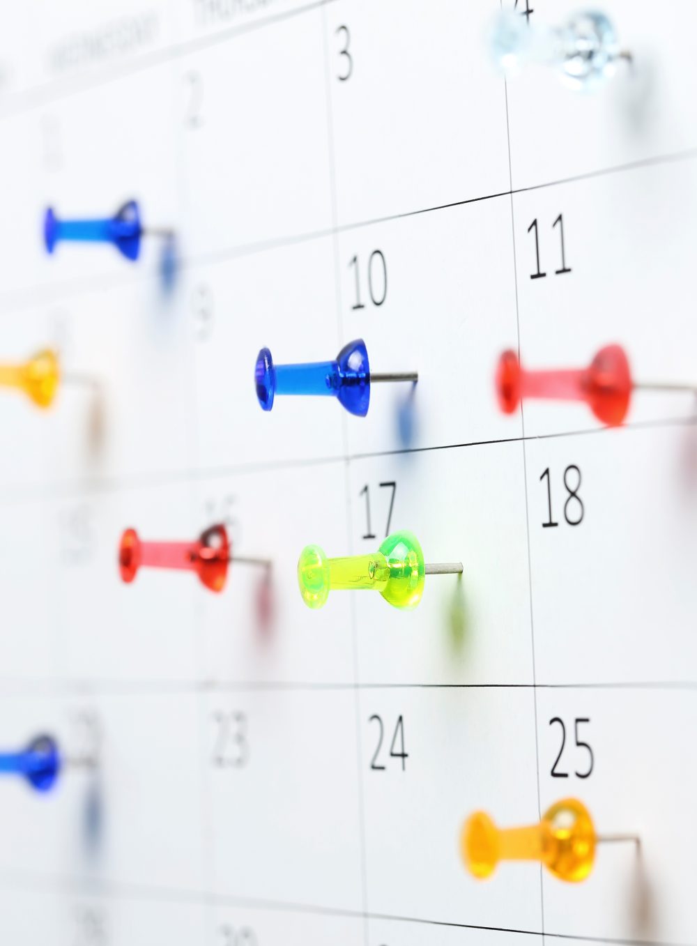 colorful pushpins on white calendar close up, shallow dof
